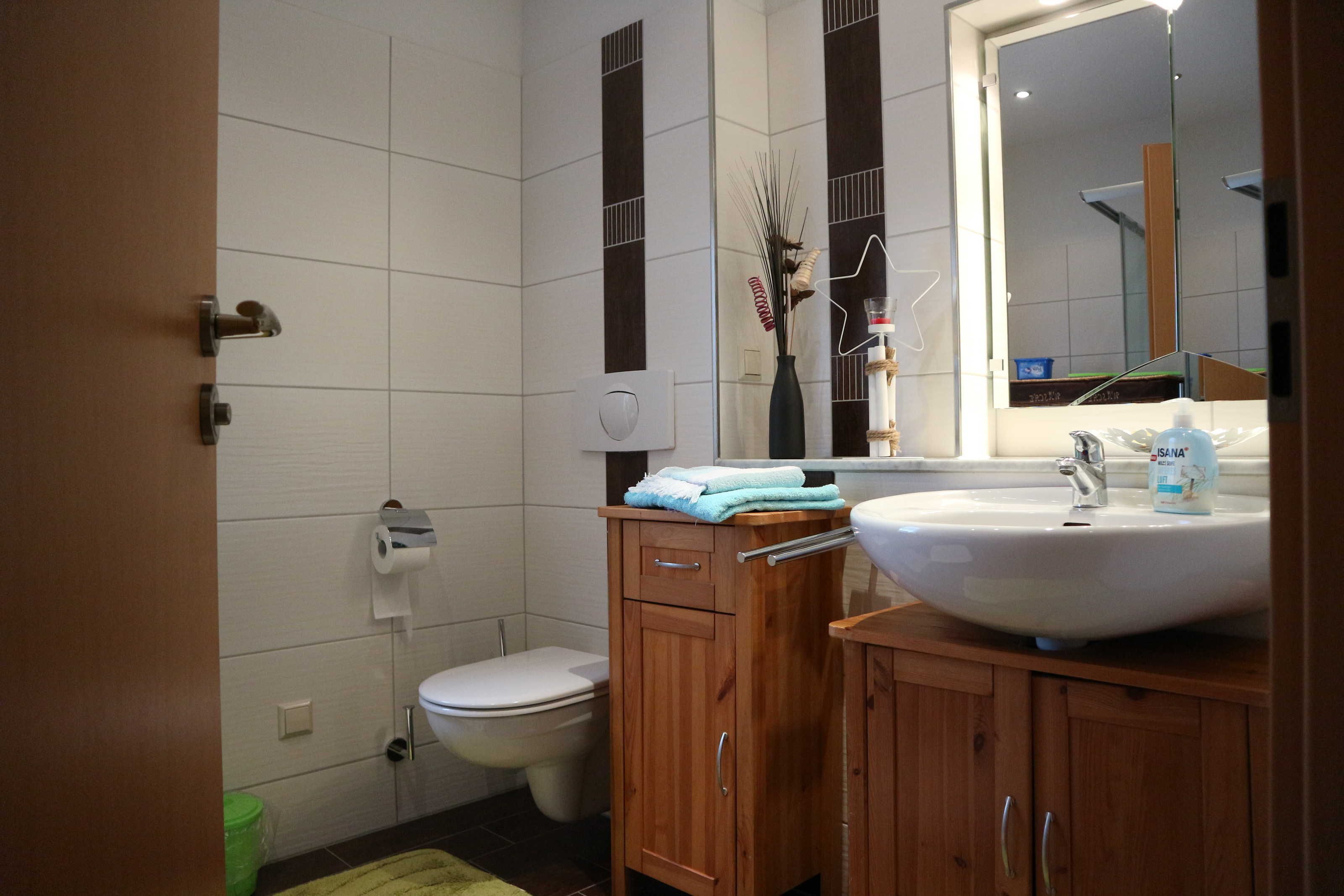 A bathroom with a toilet, sink, mirror, and wooden cabinets.