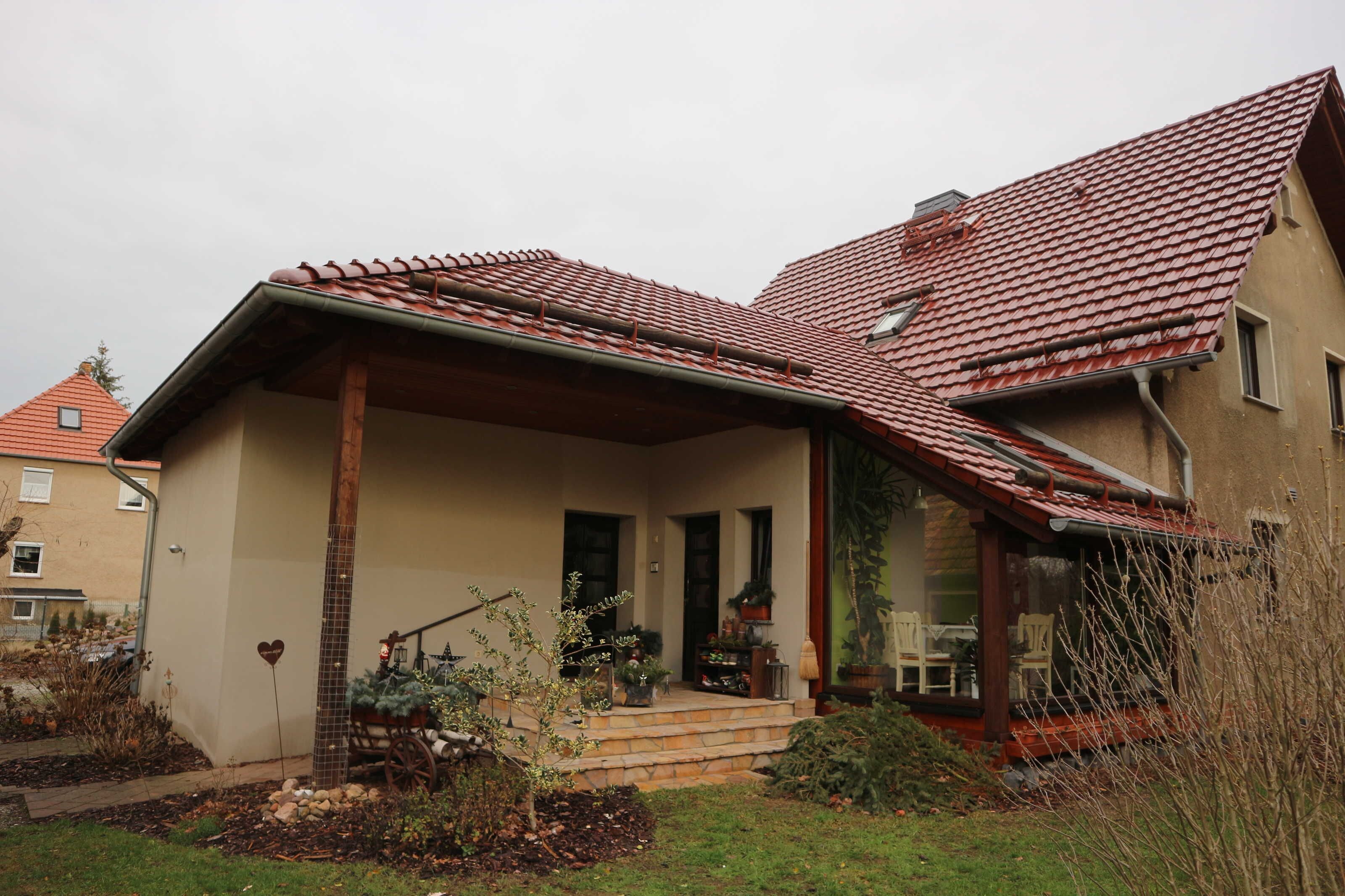A house with a sloped red-tiled roof, a front porch with steps, and a garden with plants and a heart-shaped decoration.