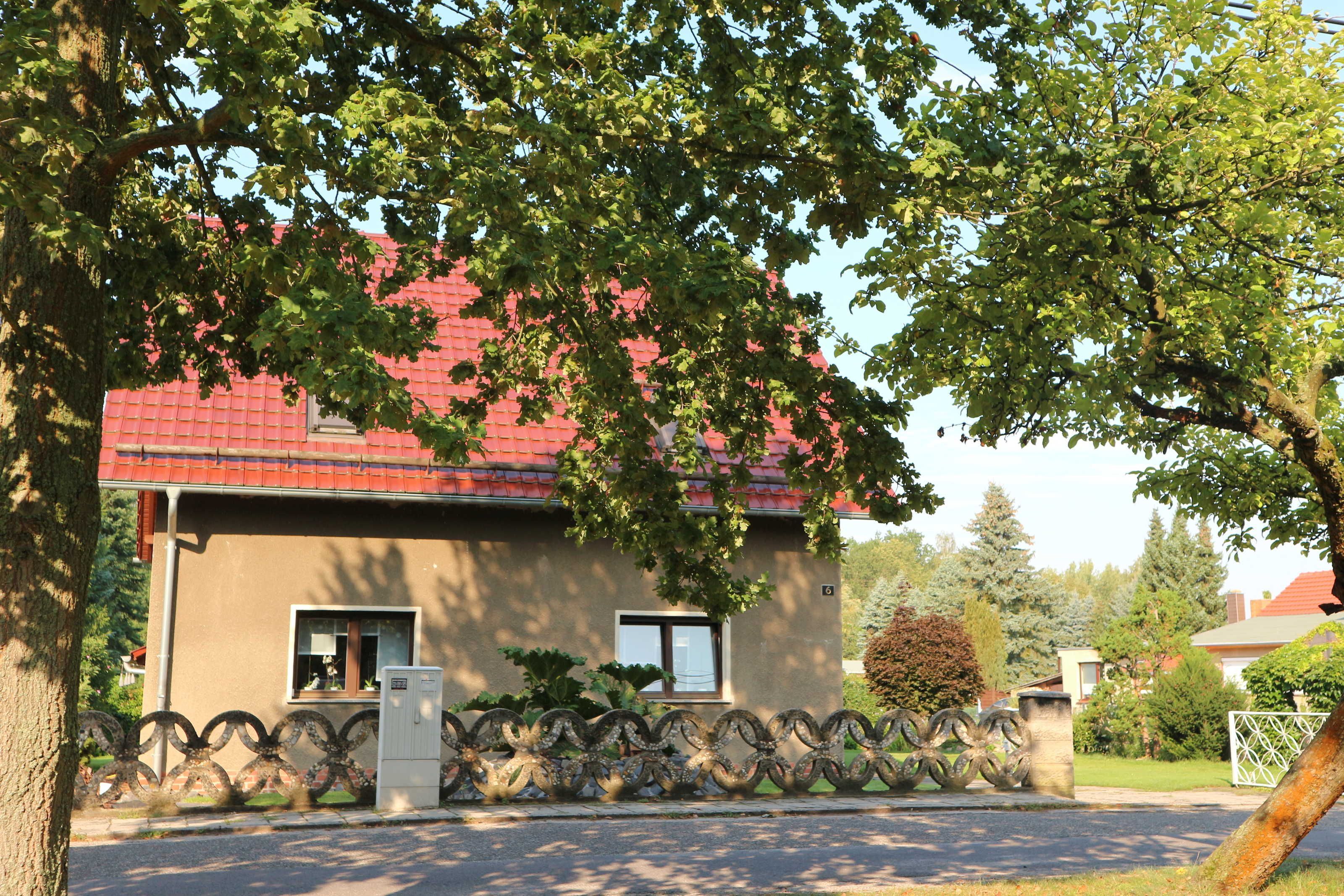 A house with a red roof, a small window, and a metal fence in front.