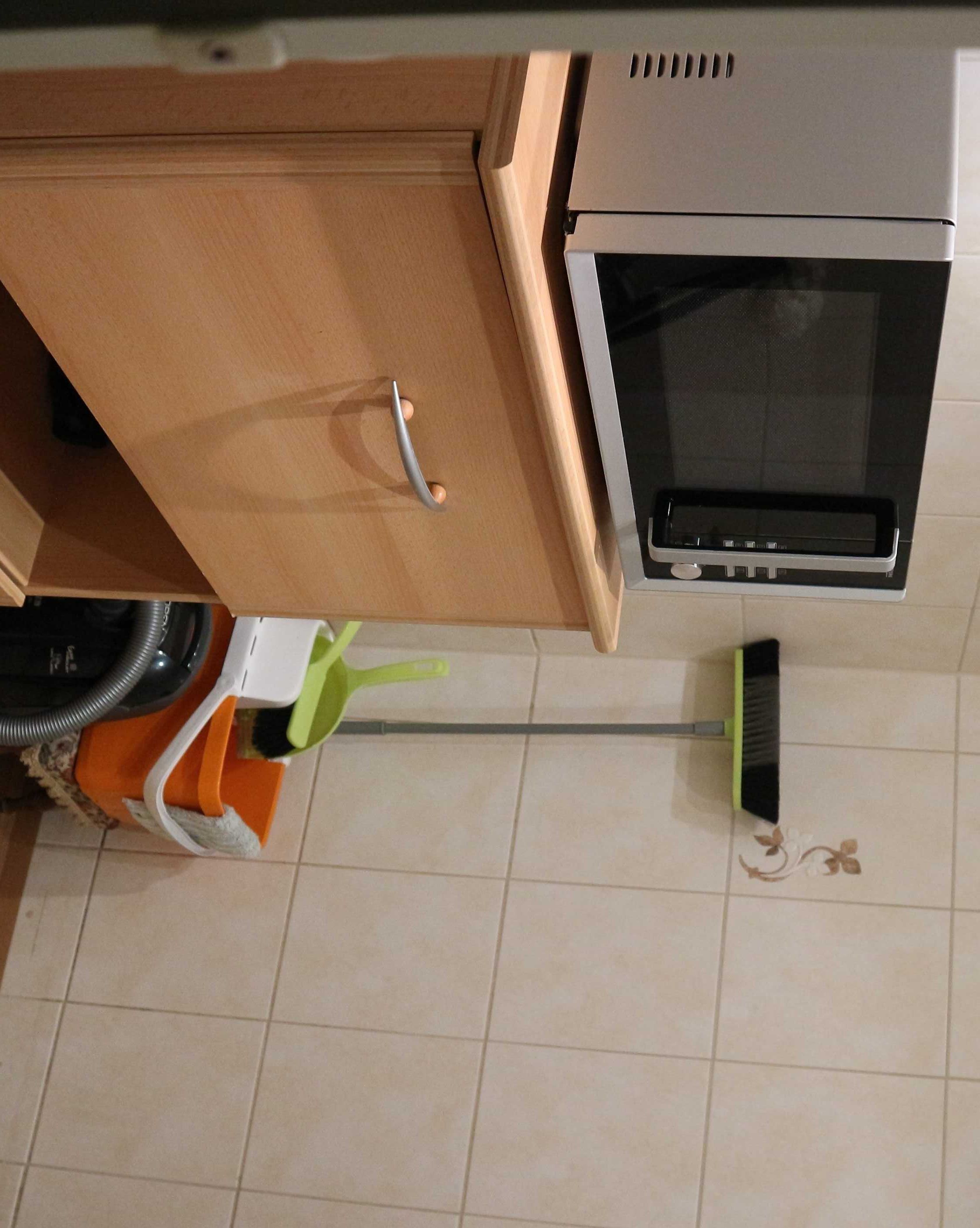 A kitchen with a microwave, a broom, and a trash bin.