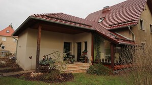 A house with a sloped red-tiled roof, a front porch with steps, and a garden with plants and a heart-shaped decoration.