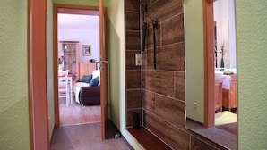 A hallway with a wooden wall, a mirror, and a door leading to a room with a bed and a desk.