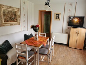 A dining area with a table, chairs, a vase with flowers, a painting, a television, and a cabinet. - Vacation apartment Big Mama's Home - Big Mama's Home (Tschernitz)