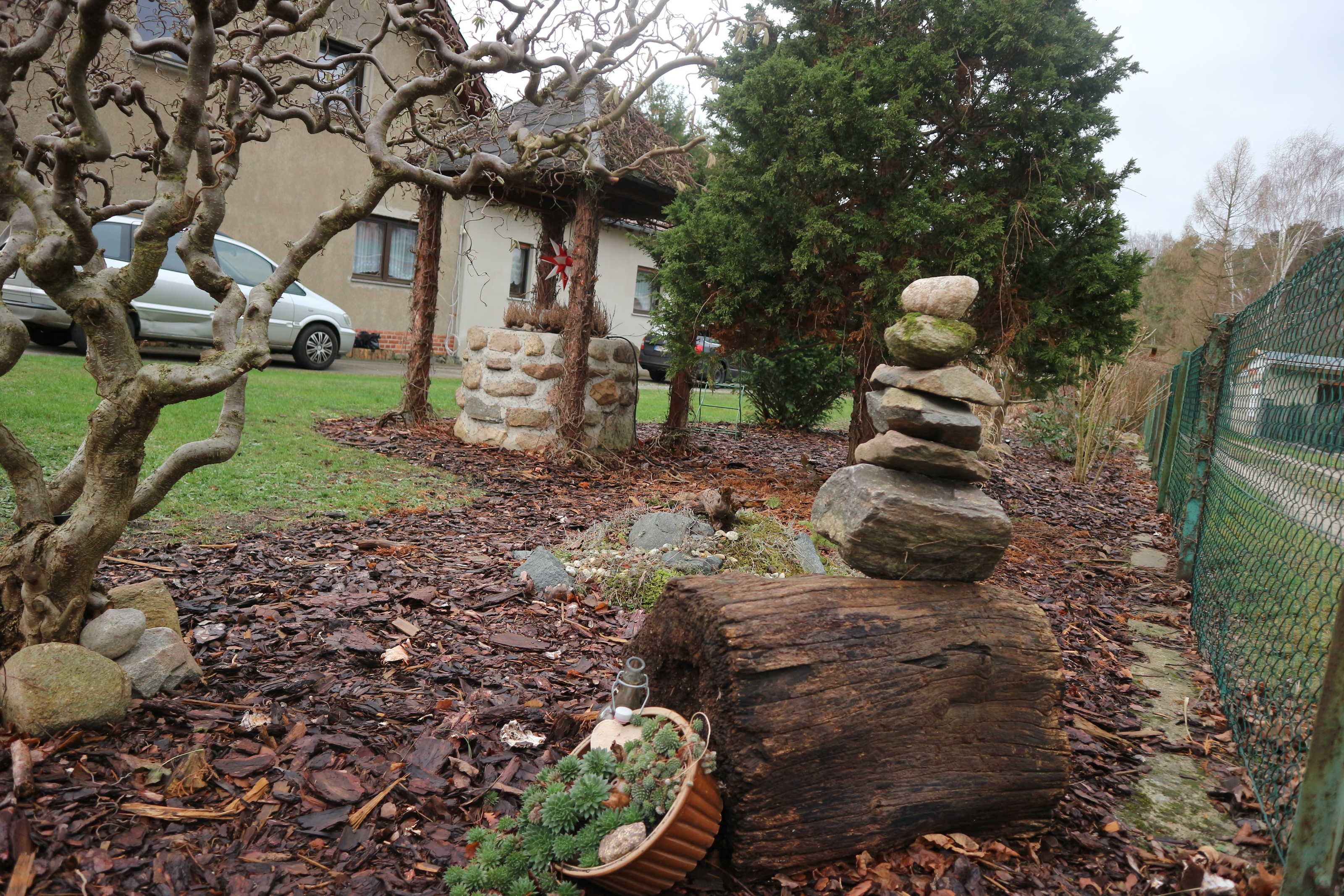 A garden with a stone structure, a wooden log, and a metal fence.