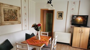 A dining area with a table, chairs, a vase with flowers, a painting, a television, and a cabinet.