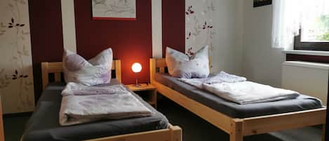 Et værelse med to senge i træ, et natbord med lampe, et billede på væggen og et vindue med udsigt.