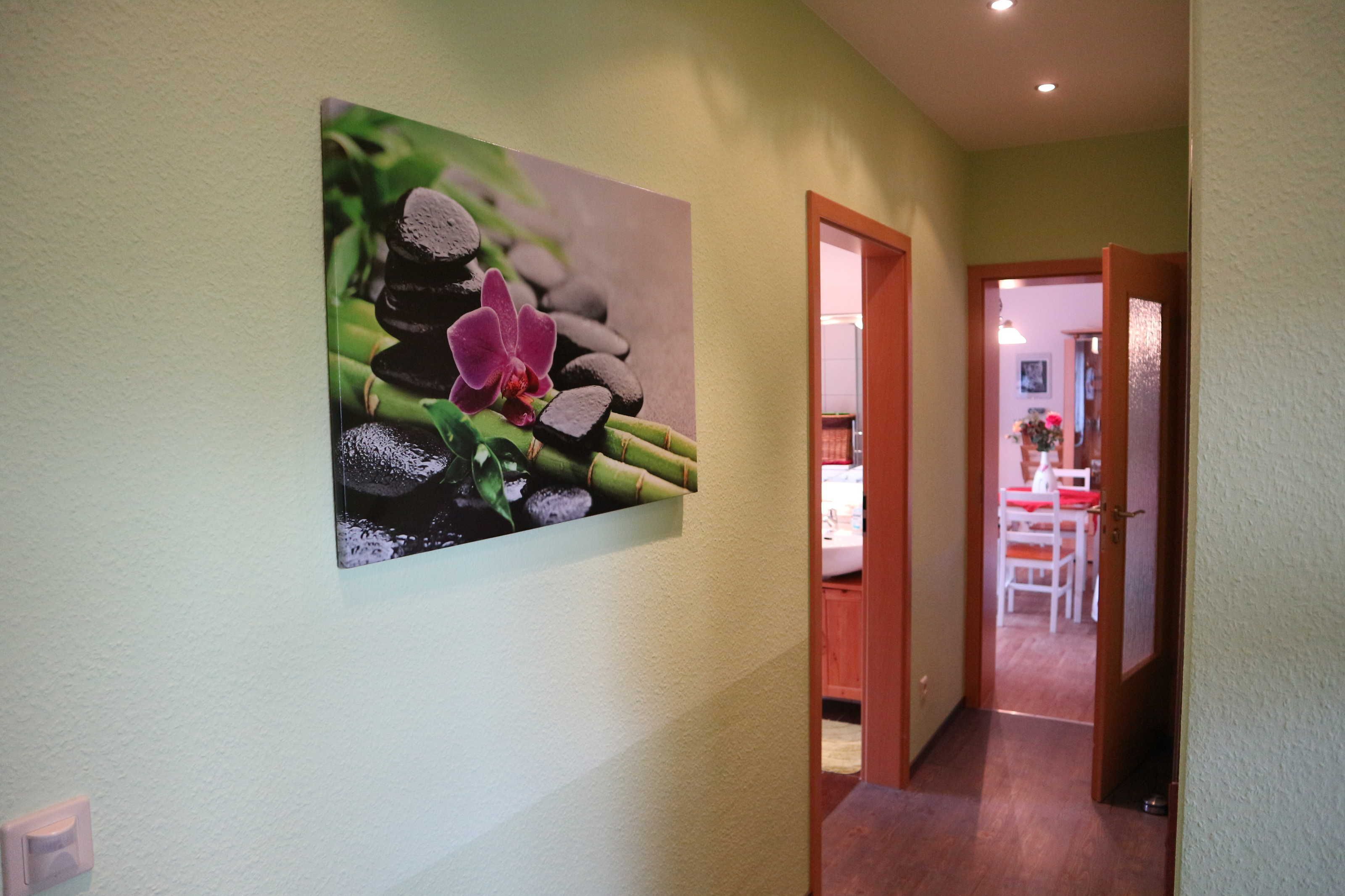 Ein Flur mit einem an der Wand befestigten Bild von einer Orchidee und Bambus, einer Holztür und einem Blick in einen Essbereich.