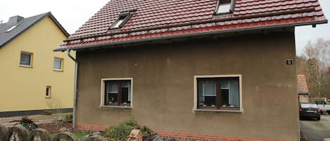 A house with a red-tiled roof, two windows, and a small porch area.