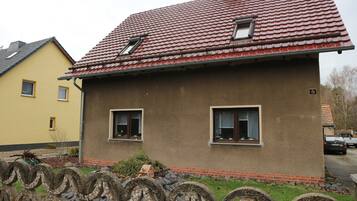 Ein Haus mit rotem Ziegeldach, zwei Fenstern und einer kleinen Veranda.