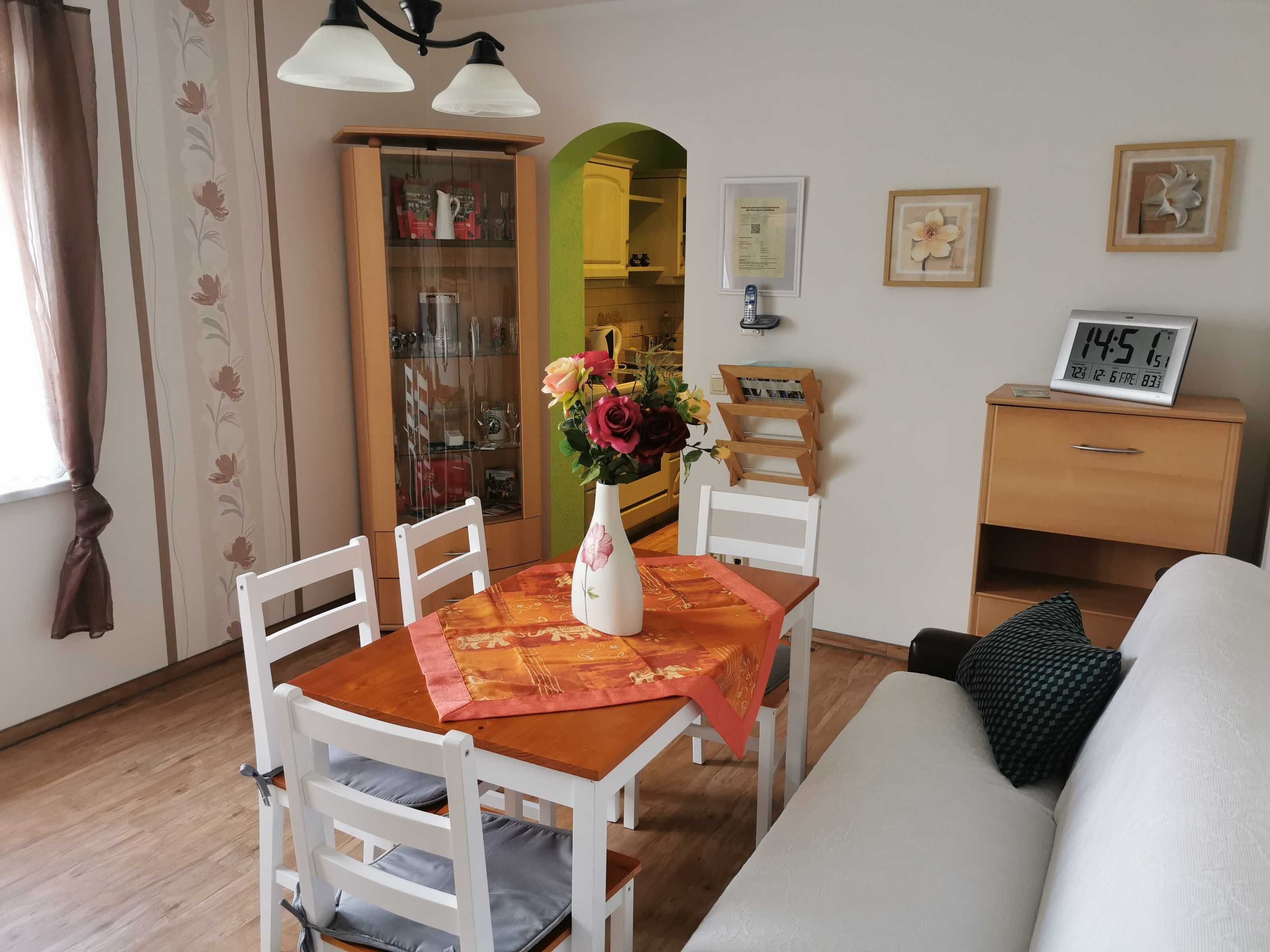 A dining area with a table, chairs, a vase with flowers, a clock, and a cabinet.
