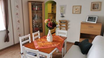 A dining area with a table, chairs, a vase with flowers, a clock, and a cabinet.