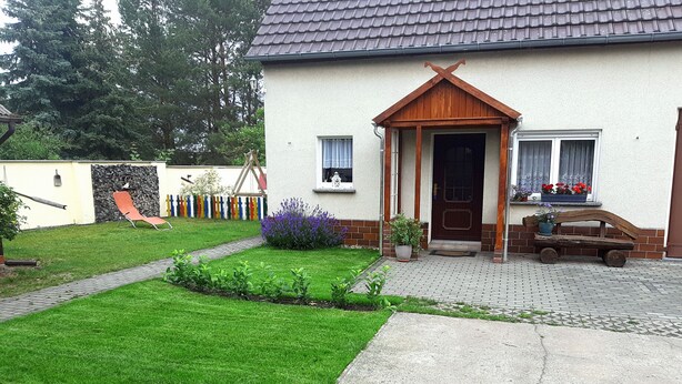 Una casa con camino pavimentado, césped y un pequeño jardín con flores.