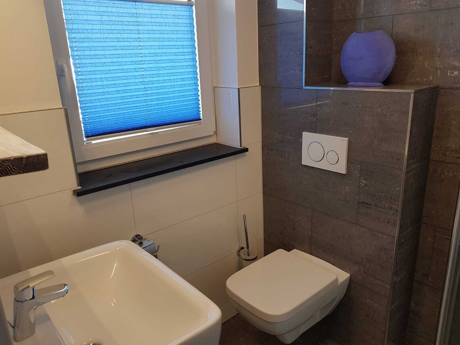 Une salle de bain avec un lavabo blanc, des toilettes et une fenêtre avec des stores.