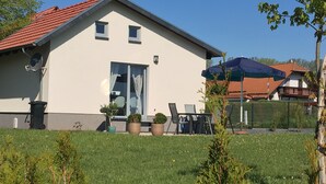 A two-story house with a red-tiled roof, a large sliding glass door, and a patio with outdoor furniture.