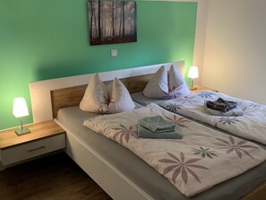 Een netjes opgemaakt bed met bloemenbeddengoed, twee nachtlampjes en een schilderij aan de muur.
