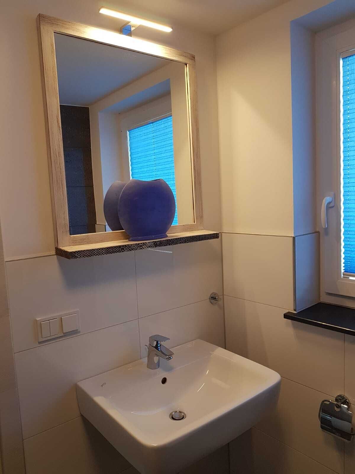 A bathroom with a white sink, a mirror with a wooden frame, and a blue vase on a shelf.