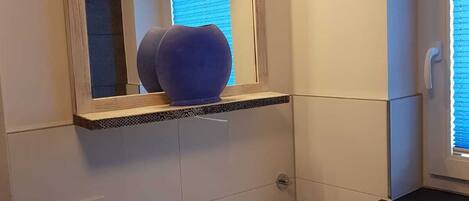 A bathroom with a white sink, a mirror with a wooden frame, and a blue vase on a shelf.