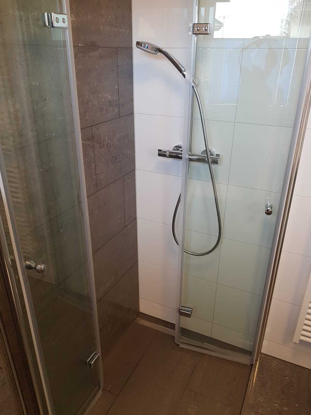 A glass-enclosed shower stall with a handheld showerhead and a wall-mounted faucet.