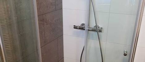 A glass-enclosed shower stall with a handheld showerhead and a wall-mounted faucet.