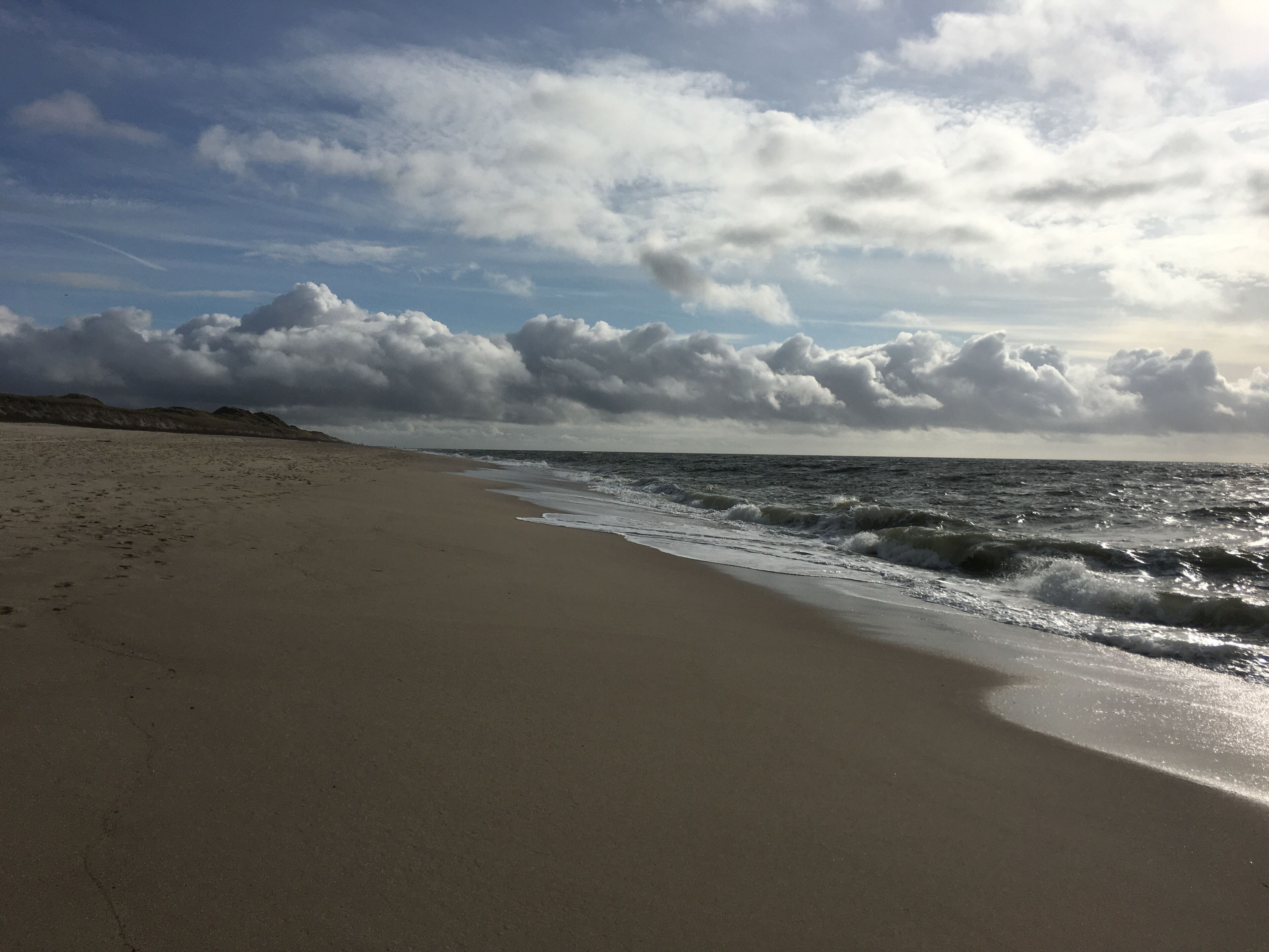 A beach with a wide sandy shore and waves approaching the beach.