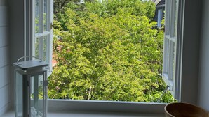 Ein Fenster mit geöffneten Klappen, ein weißer Laternen und eine Holzschale auf der Fensterbank.