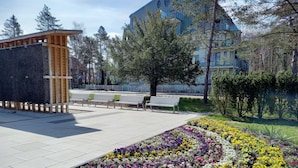 Una plaza pública con bancos, una estructura de madera y un jardín de flores.