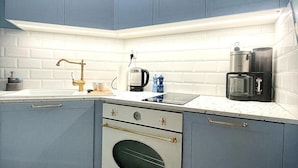Una cocina con gabinetes azules, encimera blanca, cafetera de acero inoxidable y horno de estilo vintage.