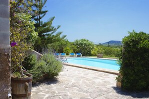 A stone-paved pool area with blue lounge chairs and lush greenery. - Traditional Finca Era des Pou, private pool, quiet location, large garden, Wi-Fi (Felanitx)