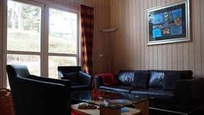 A living room with a black leather sofa, two armchairs, a glass coffee table, and a large window with curtains. - House in the dunes (Mecklenburg Vorpommern)