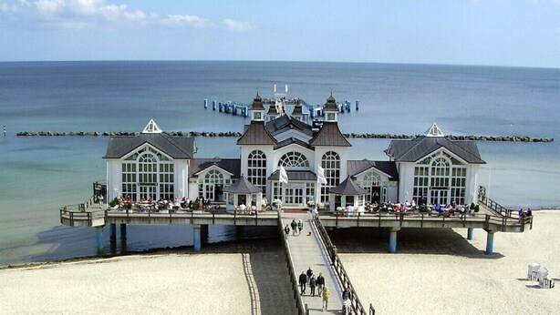 A large, white, multi-story building with a central tower, located on a pier extending into a calm sea. - House in the dunes (Mecklenburg Vorpommern)