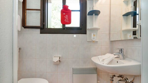 Baño con inodoro, lavamanos y ventana con un objeto con forma de corazón rojo colgando.