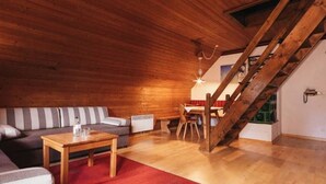 A cozy living room with a wooden ceiling, a staircase, a sofa, a coffee table, and a dining area. - Apartment of the SÜDsee 1 - Naturel Hoteldorf SEELEITN (Faak am See)