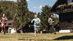 A group of children playing in a grassy area with a wooden cabin in the background. - Apartment of the SÜDsee 1 - Naturel Hoteldorf SEELEITN (Faak am See)