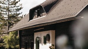 A rustic log cabin with a steeply pitched roof, a small dormer window, and a front door with a green frame. - Apartment of the SÜDsee 1 - Naturel Hoteldorf SEELEITN (Faak am See)