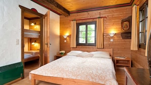 A wooden cabin bedroom with a bunk bed, a large bed, and a window with curtains. - Apartment of the SÜDsee 1 - Naturel Hoteldorf SEELEITN (Faak am See)