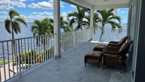A covered balcony with a view of the sea, featuring wicker chairs and a white railing. - *** Luxurious Villa at River ***  (Florida)