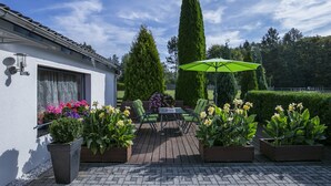 Een terras met een tafel en stoelen, omringd door potplanten en een groene parasol.