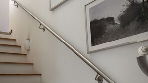 A staircase with wooden steps, a metal handrail, and framed pictures on the wall. - House at the sea (Wohlenberg)