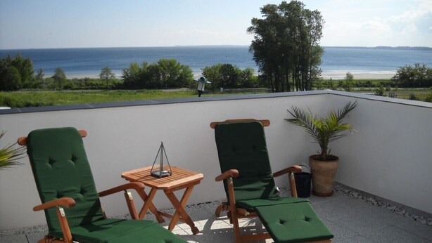 A terrace with two green cushioned chairs, a small wooden table, and a potted plant. - House at the sea (Wohlenberg)