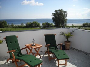 A terrace with two green cushioned chairs, a small wooden table, and a potted plant. - House at the sea (Wohlenberg)
