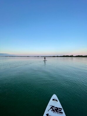 Ruhiges Gewässer, in der Ferne steht eine Person auf einem Stand-Up-Paddleboard.