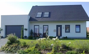 Ein modernes, zweigeschossiges Haus mit dunklem Dach, Garage und einem gepflegten Garten mit weißen Blumen.