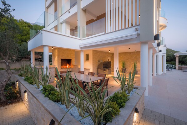 A modern two-story house with a patio, outdoor seating, and a fireplace.