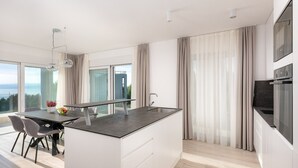 A modern kitchen with a central island, a dining area with chairs, and large windows offering a view. - Villa 01 - Apartment 4 (4 + 2, 2nd floor) (Promajna)