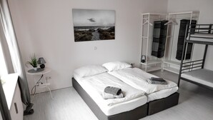 Une chambre moderne avec un grand lit, une table de chevet avec une lampe, une petite plante en pot, un tableau accroché au mur et une structure de lit superposé.