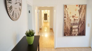 Un couloir avec une horloge, une porte portant l’inscription « 6 », et un tableau encadré accroché au mur.