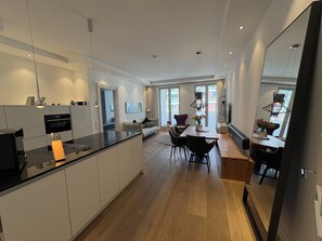 A modern kitchen with a central island, dining area with a wooden table and chairs, and a living space with a sofa and a TV.