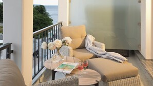 Un balcon avec un canapé, une petite table sur laquelle est posé un magazine et deux verres de vin rouge, ainsi qu’une chaise en osier.