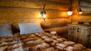 Une chambre chaleureuse dans un chalet en rondins, avec un lit recouvert de fourrure, des murs en bois et deux lampes fixées au mur.