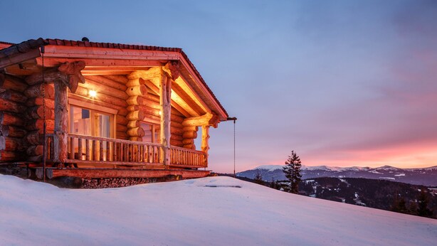 Une cabane en rondins dotée d’un balcon donnant sur un paysage enneigé, avec des montagnes en arrière-plan.